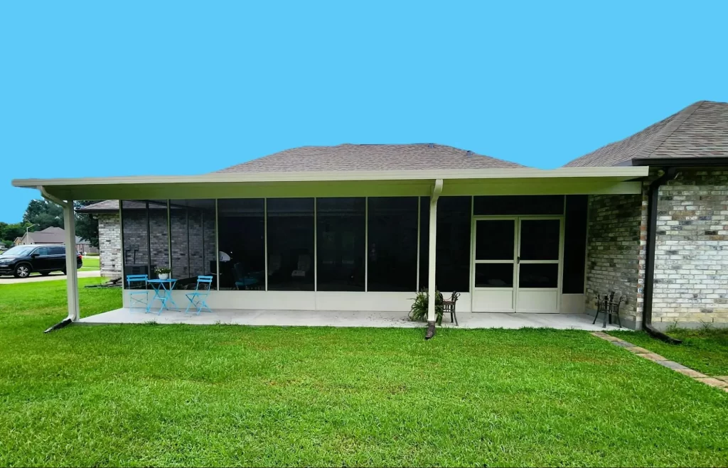 A brick house with a screened-in porch. The porch has a table set with four blue chairs and overlooks a green lawn. The roof is sloped.