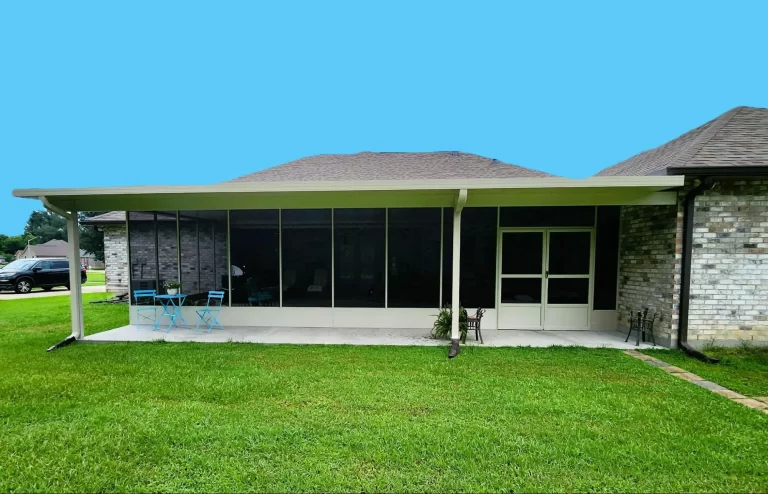A brick house with a screened-in porch. The porch has a table set with four blue chairs and overlooks a green lawn. The roof is sloped.